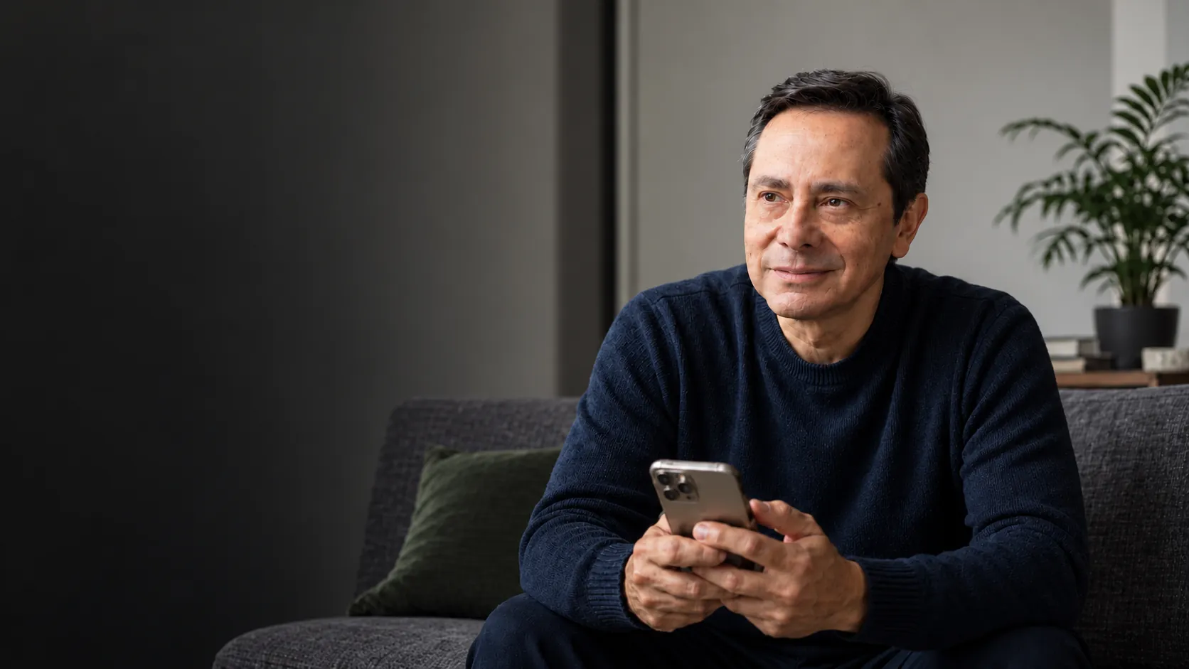 A man sitting on a sofa holding a phone in a quiet, reflective moment